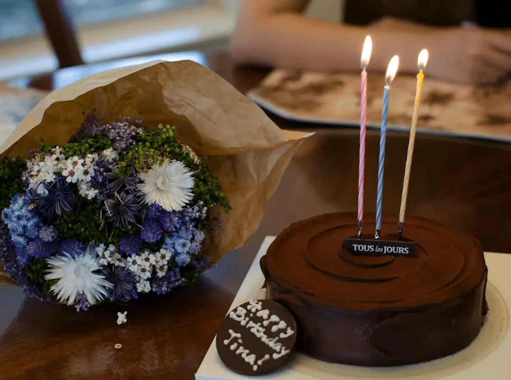 A birthday cake and a flower bouquet can be seen